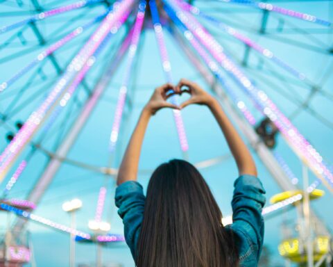 girl lifting his hands in a carnival with his back facing the camera