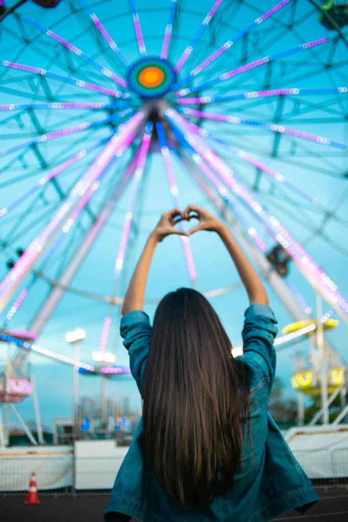 girl lifting his hands in a carnival with his back facing the camera