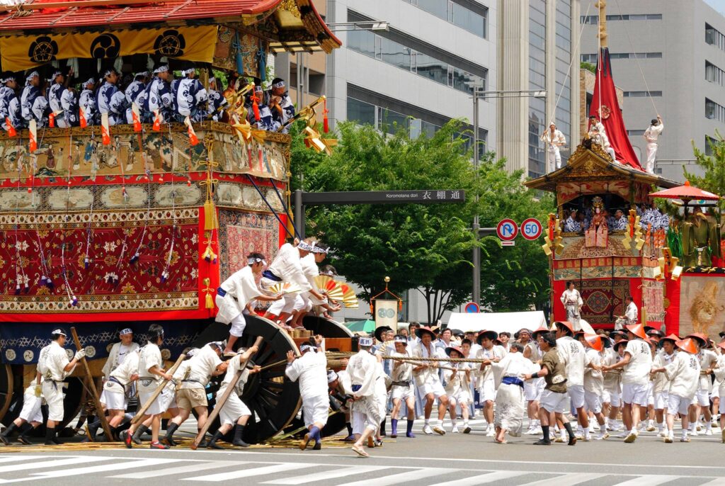 Picture of a group of men wearing white, pulling a big wagon through the streets of Kyoto during the Gion Matsuri festival