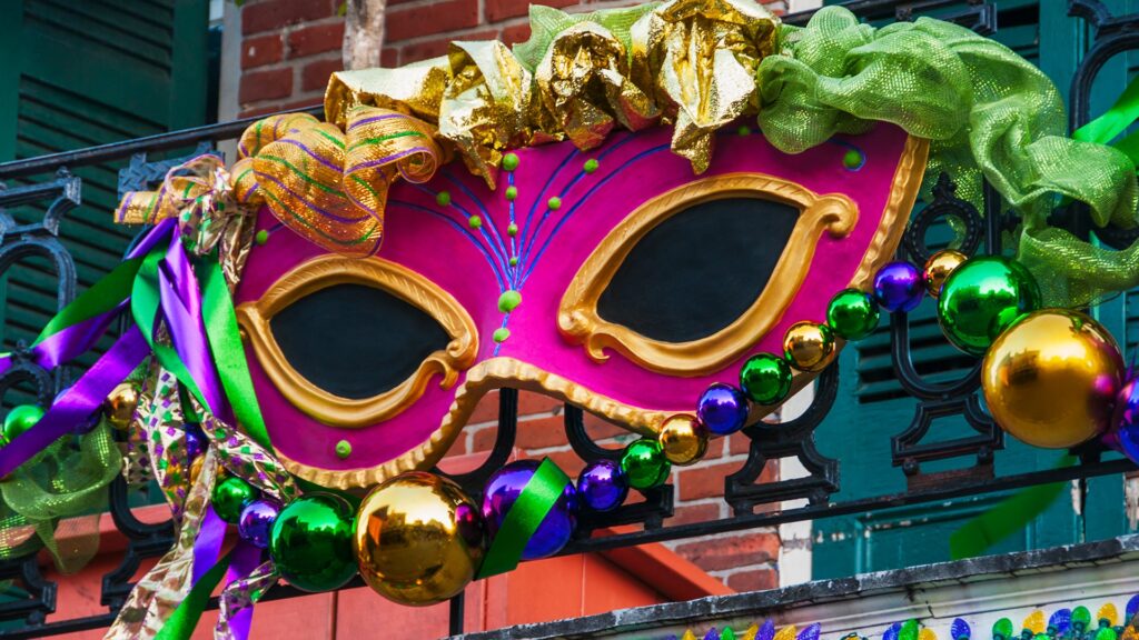 Picture of a huge party mask hanging off a balcony in new Orleans during the Mardi Gras festival