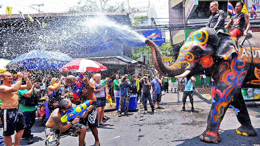 Picture of two men riding a painted elephant that is spraying a group of people on the streets during the Songkran festival