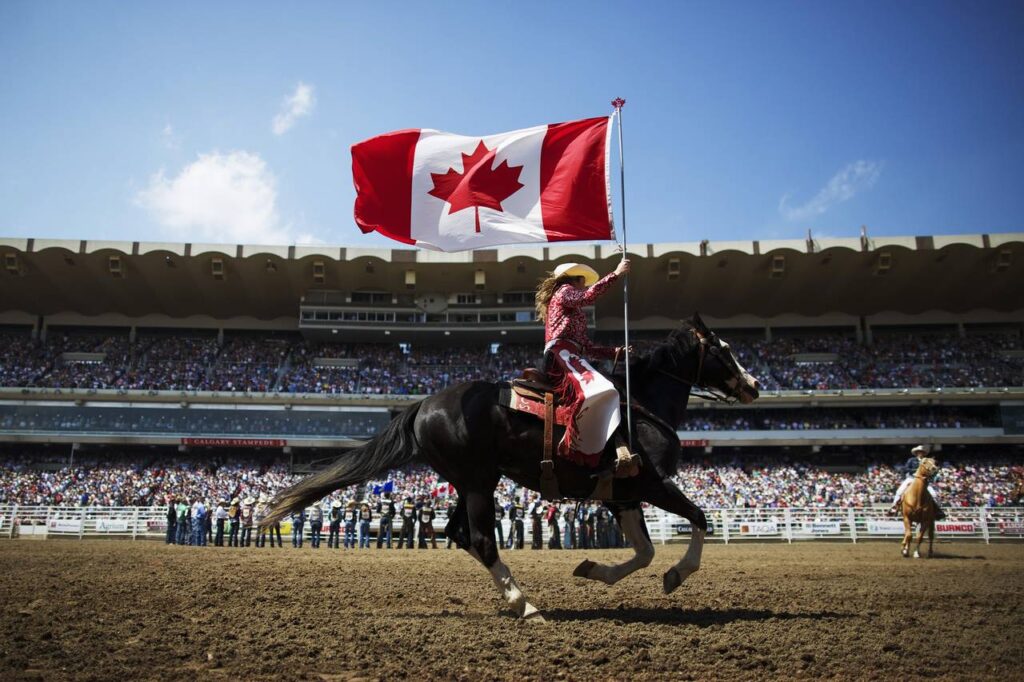 Men riding a horse while hoisting a Canadian flag during the Calgary Stampede